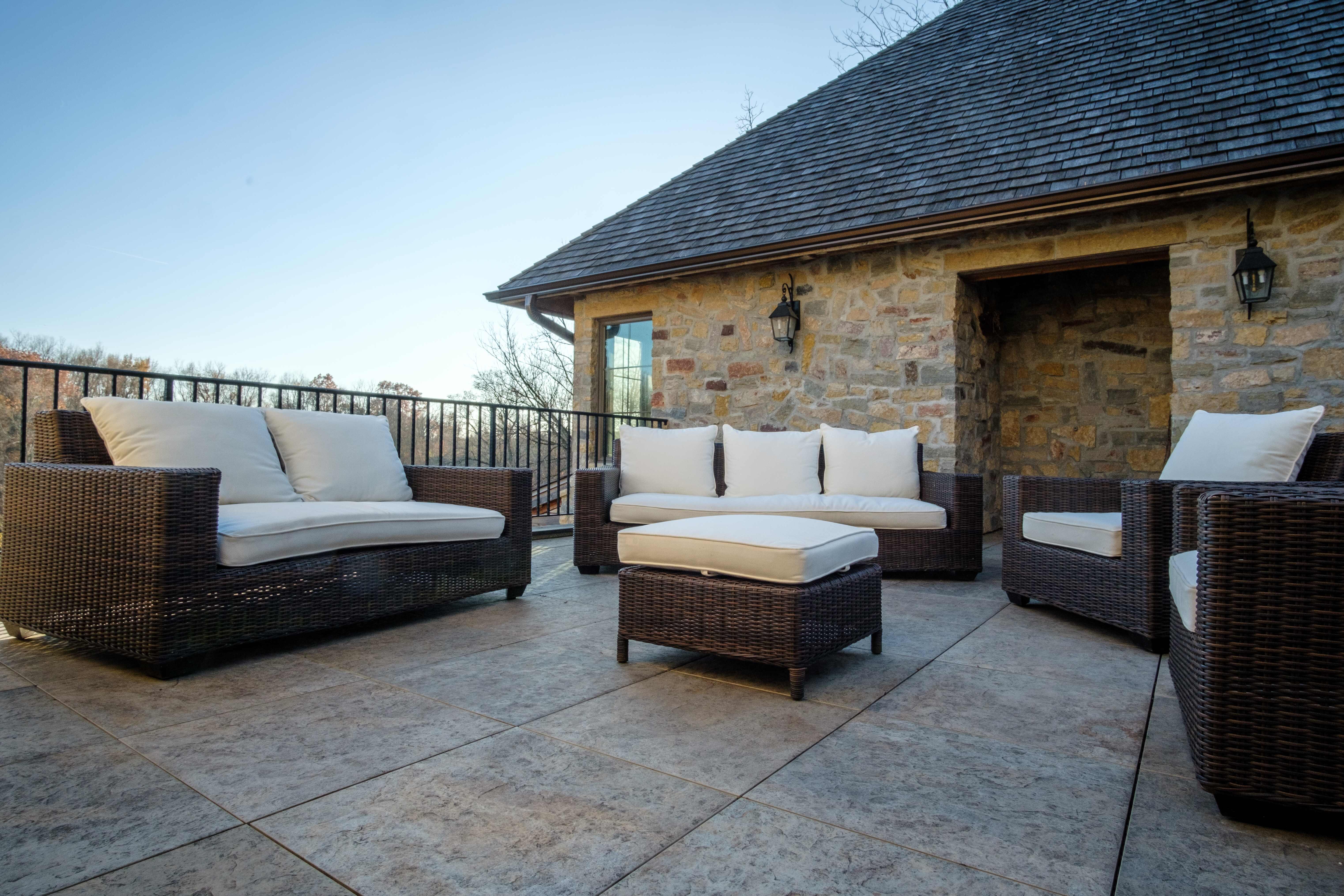 Mbrico Tile patio with wicker furniture set, featuring cushioned seating and a stone wall backdrop, perfect for relaxation and entertaining.