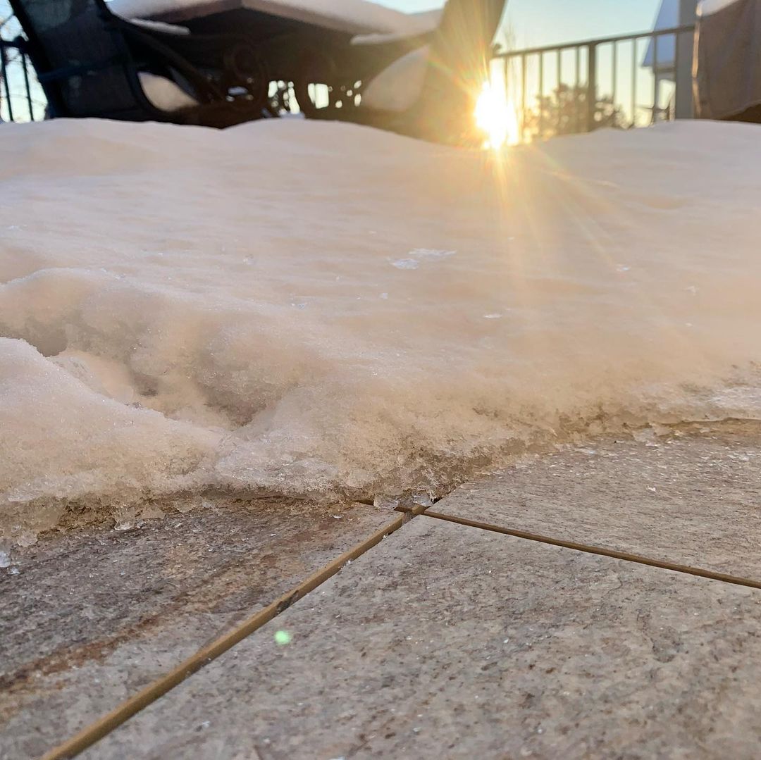 Snow-covered Mbrico Tile patio with sunlight shining through outdoor furniture, highlighting the icy surface. Winter morning scene on a tiled terrace.