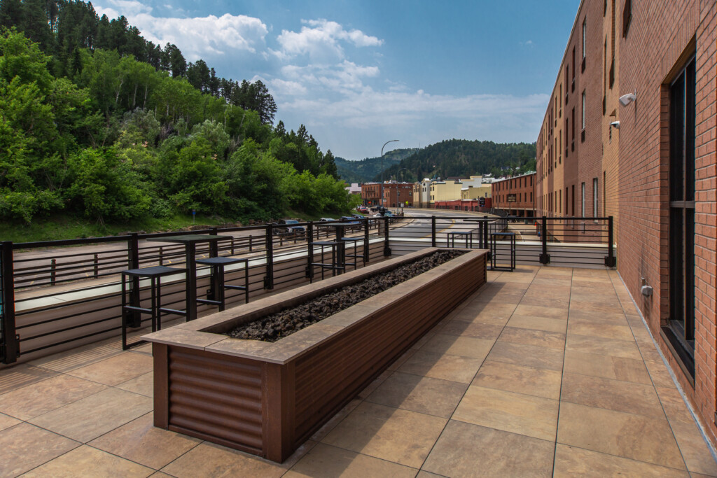 Hospitality rooftop terrace featuring Mbrico reinforced porcelain pavers, a linear fire feature, outdoor seating, and views of Deadwood, South Dakota.