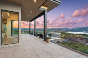 Covered residential terrace featuring Mbrico reinforced porcelain pavers, glass railings, and panoramic mountain and lake views at sunset.